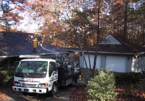 Pressure washing a residential roof to remove dirt, algae, and debris.